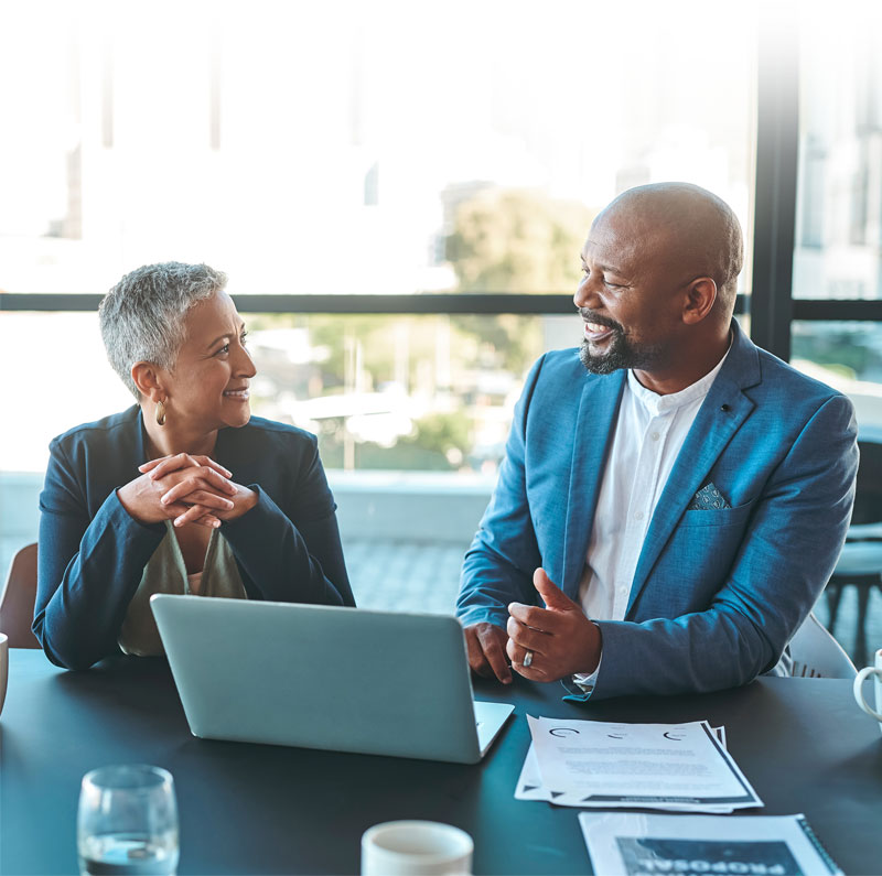 financial advisor talking to a client at a table with a laptop, papers, and coffee cups